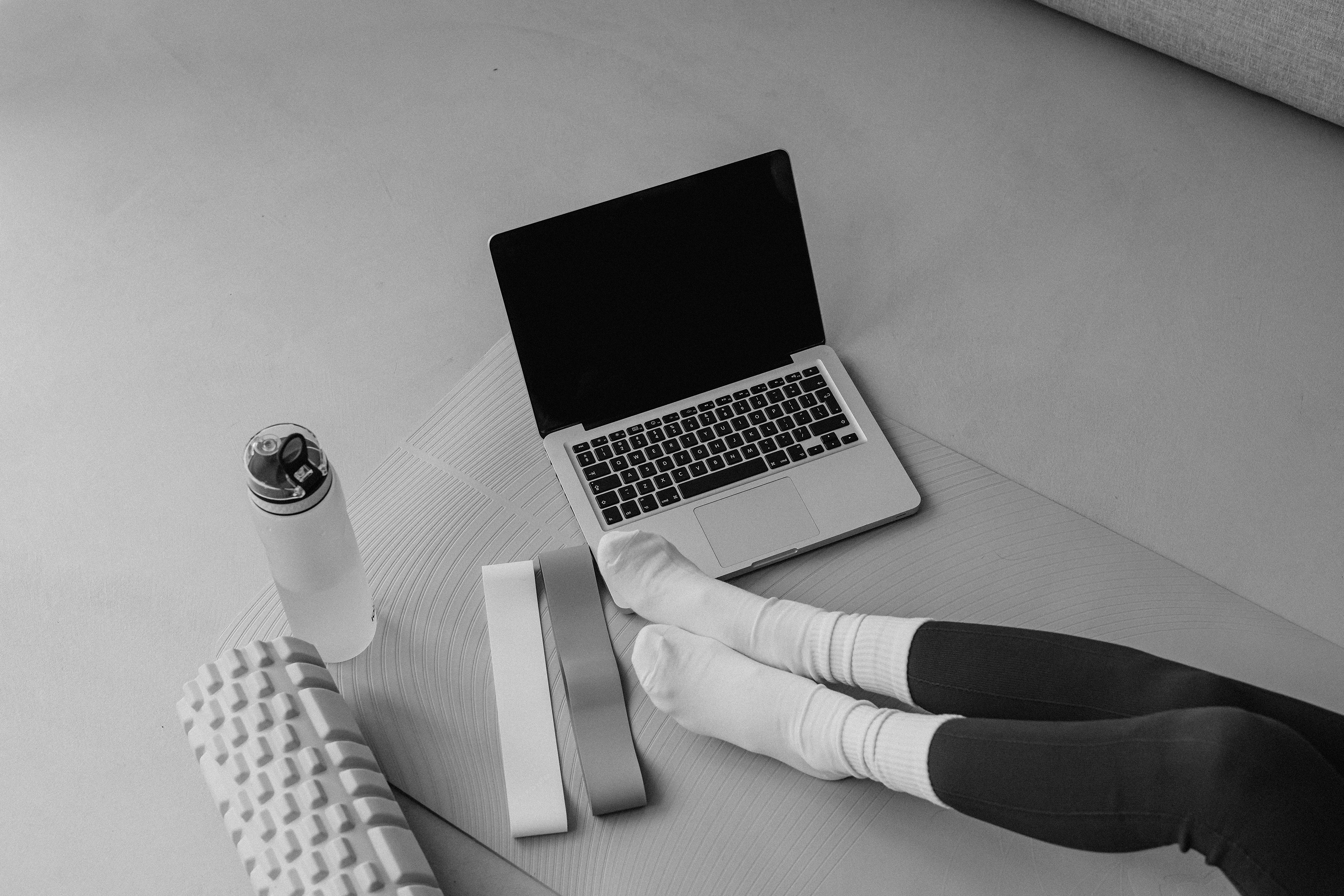 A person wearing socks and leggings sits on a mat near a laptop, water bottle, foam roller, and resistance bands in a historic apartment in the Cabana Design District.