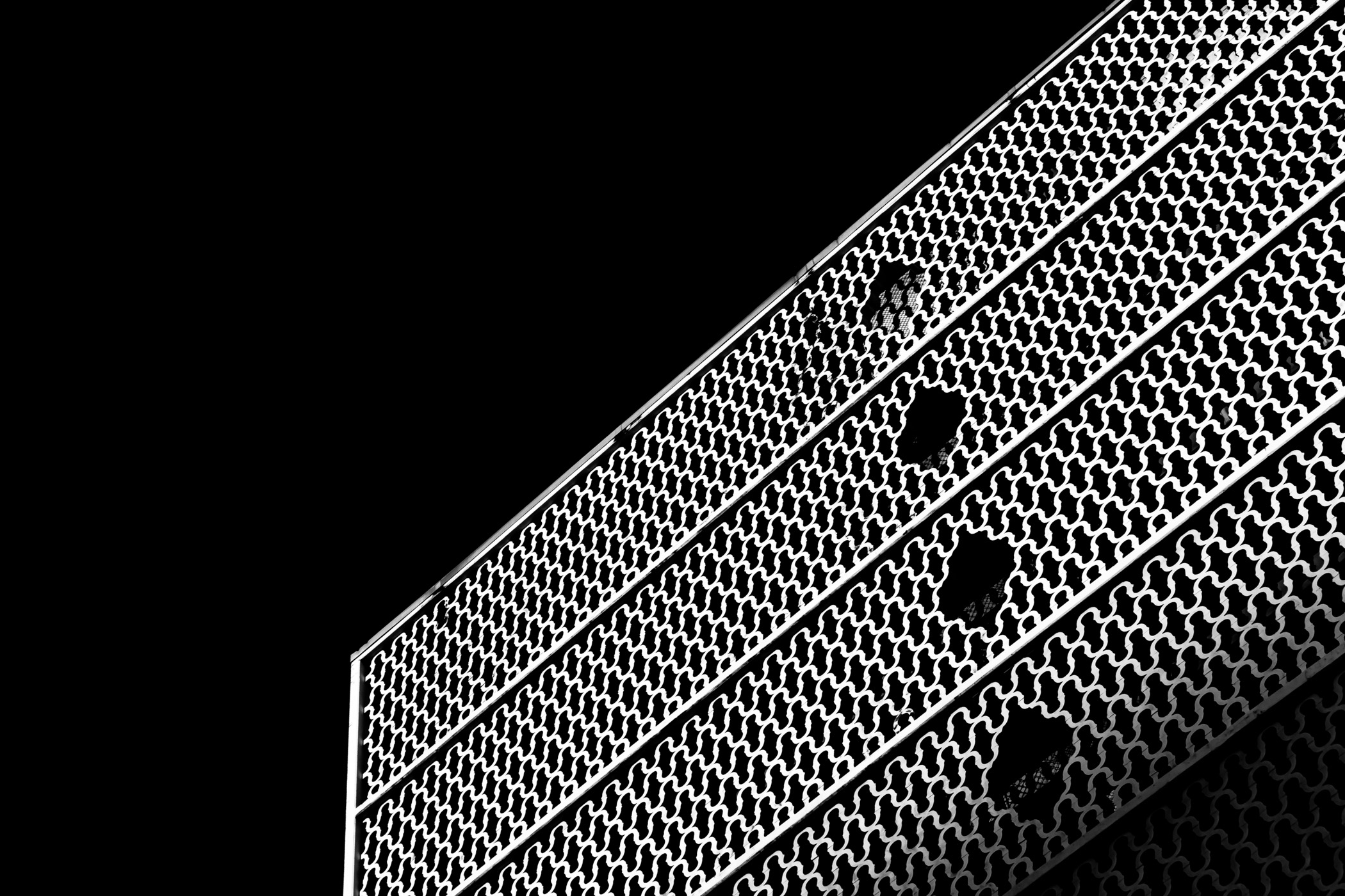 Close-up of a building facade in the Cabana Design District, Dallas, featuring a geometric, lattice-like pattern with several irregular holes, shown against a black background.