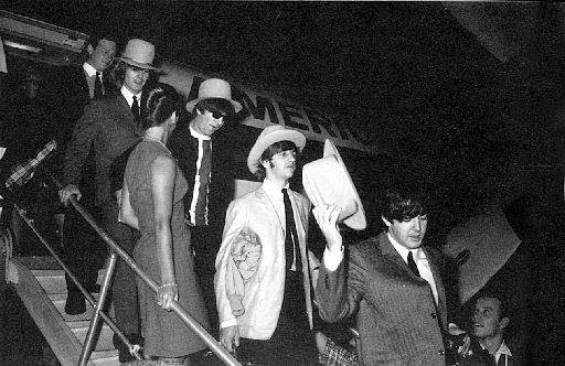A group of men in suits and hats walk down airplane stairs in this historic scene, with part of an aircraft and its logo visible in the background.