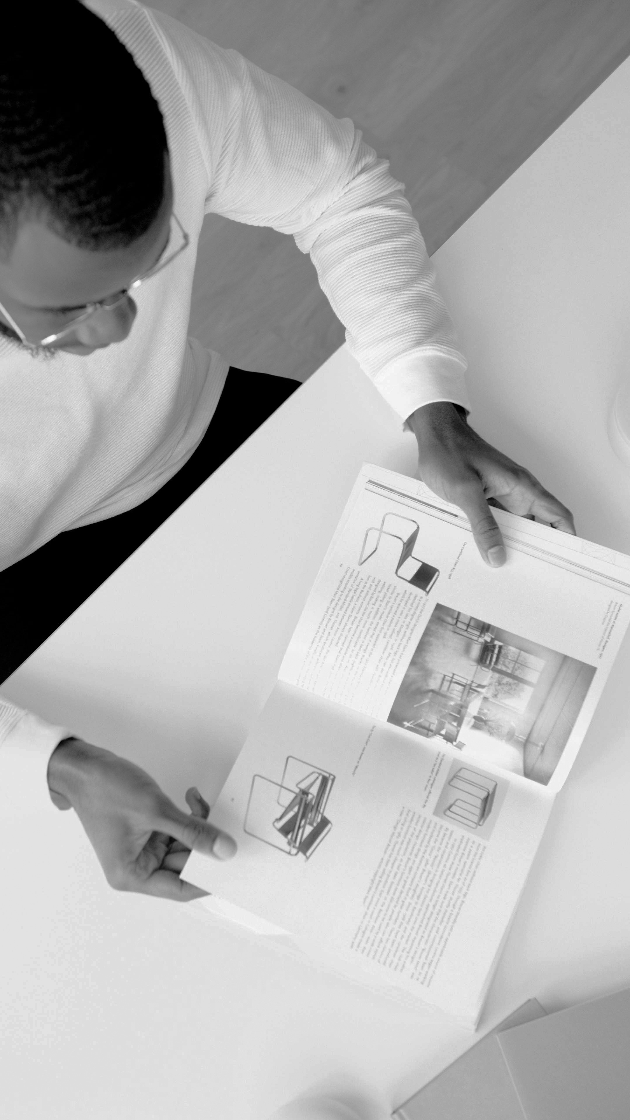 Person reading a book with images and text, seated at a white table in a Dallas apartment, viewed from above.
