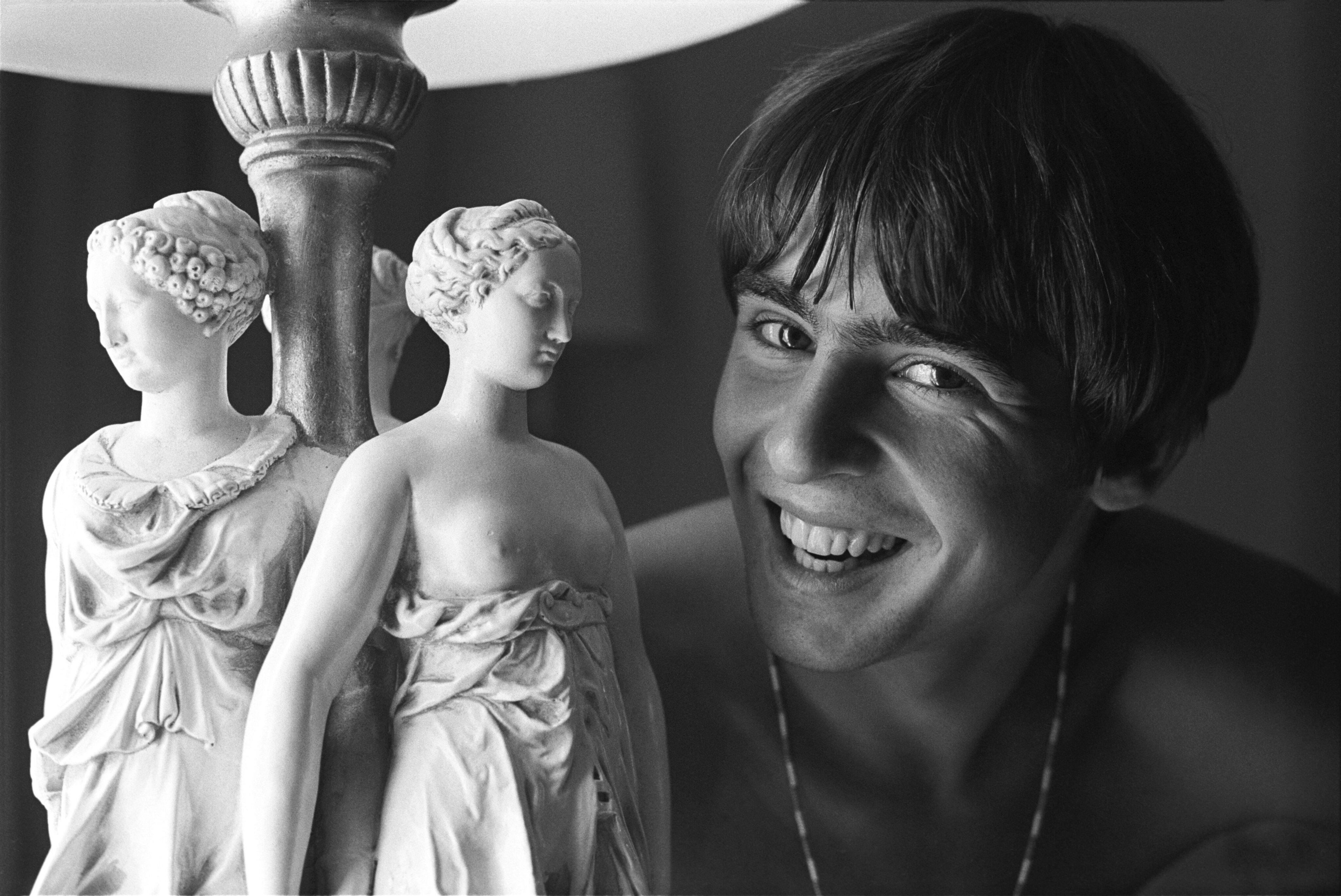 A smiling young man poses next to a lamp featuring two sculpted female figures in classical-style dresses, adding a touch of historic elegance often found in Dallas apartments.
