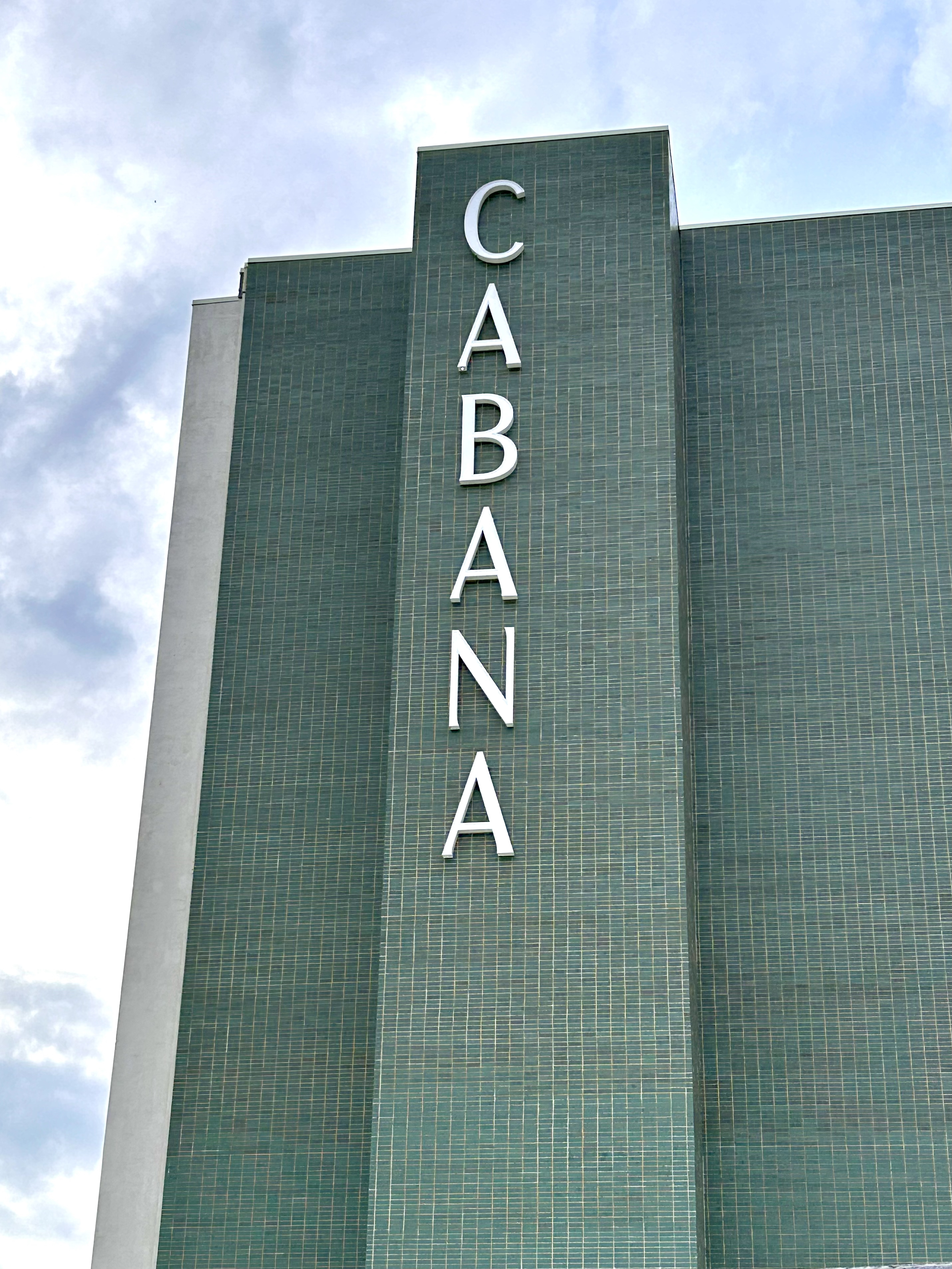 Green-tiled building facade with the word "CABANA" spelled vertically in large white letters against a partly cloudy sky—a standout among Dallas Apartments.