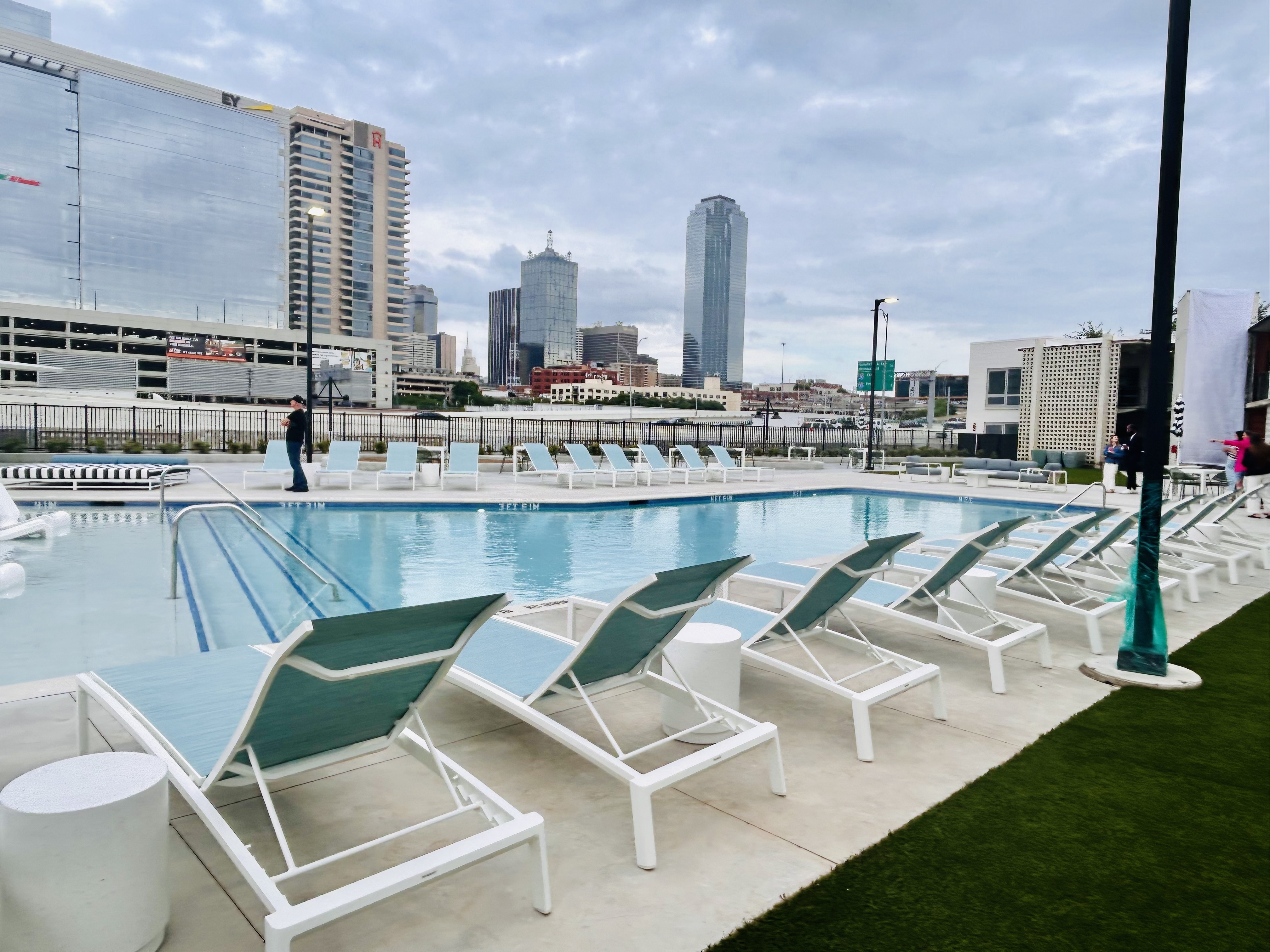 Outdoor swimming pool with white lounge chairs, set against a city skyline and cloudy sky—enjoy modern Dallas Rental apartments in a vibrant, historic setting.