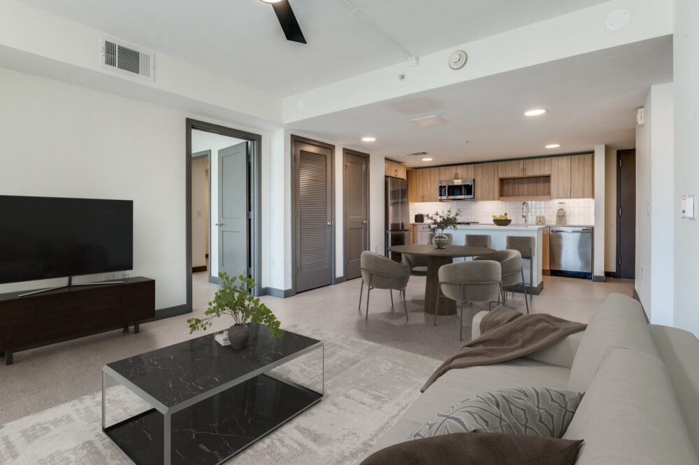 Modern Dallas Rental with a spacious living room and kitchen area featuring a sofa, coffee table, TV, dining table, and stainless steel appliances. Neutral tones and minimalistic decor define this Cabana Design District home.