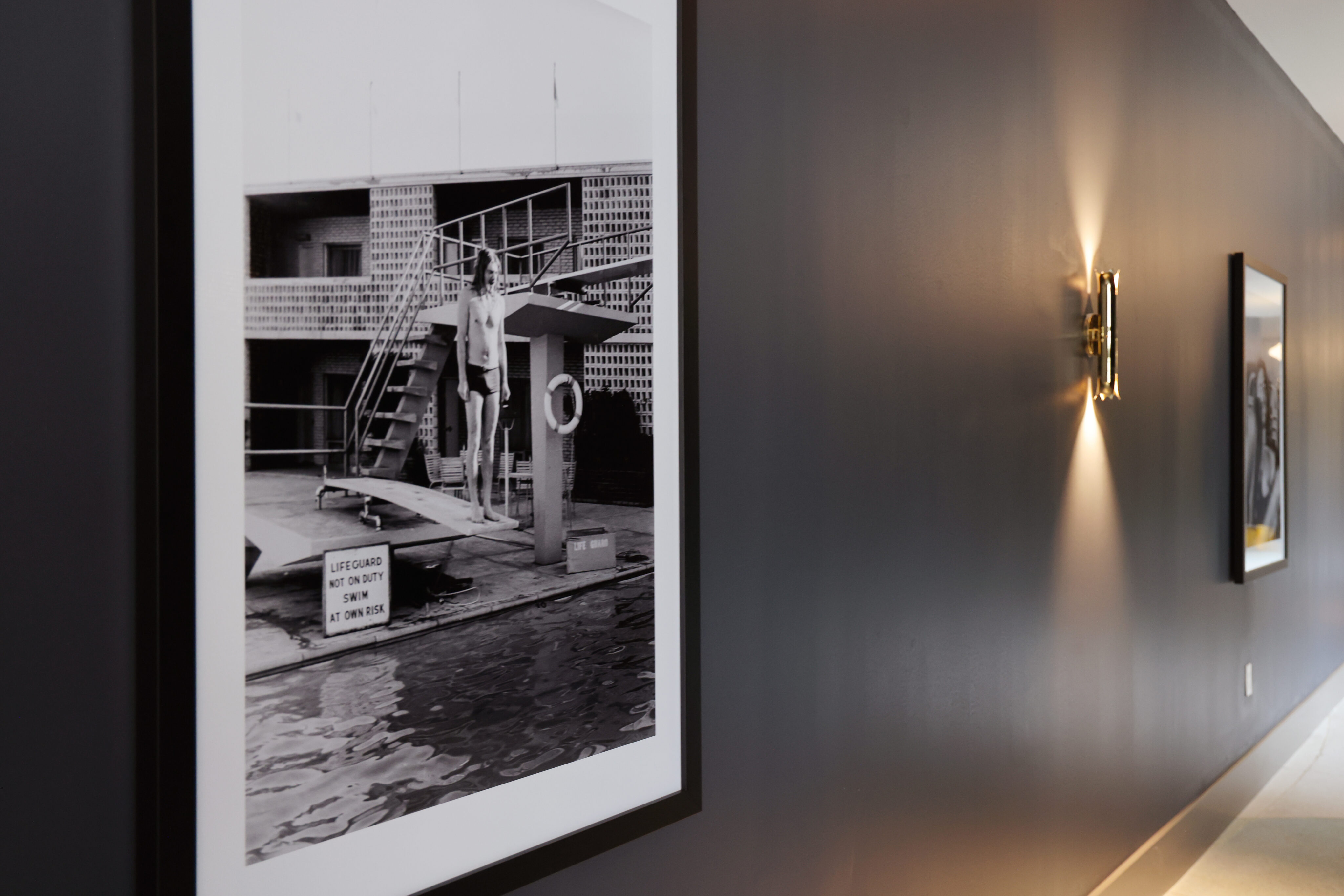 Black-and-white photo of a lifeguard on a platform by a pool, framed and mounted on a dark hallway wall with modern lighting—adding a touch of historic charm to upscale Dallas rental apartments.